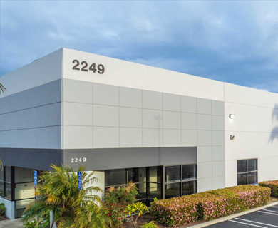 Exterior view of a modern, gray commercial building with the number "2249" prominently displayed, surrounded by green landscaping.