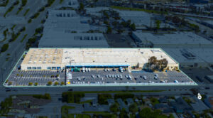 Aerial view of a large retail building with a spacious parking lot filled with cars, surrounded by industrial and commercial areas.