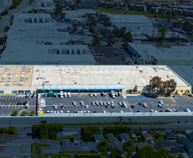 Aerial view of a large retail building with a spacious parking lot filled with cars, surrounded by industrial and commercial areas.